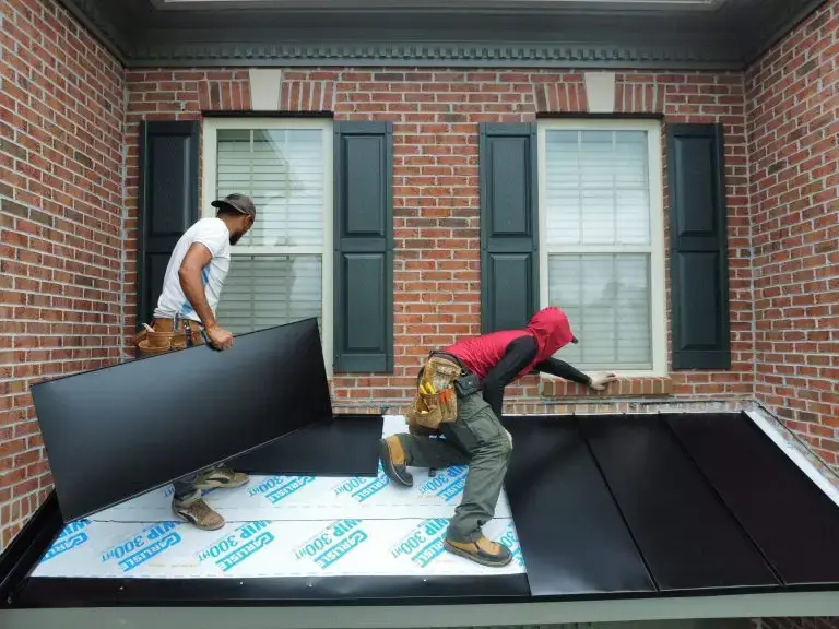 Workers fitting metal roof panels beside a brick wall