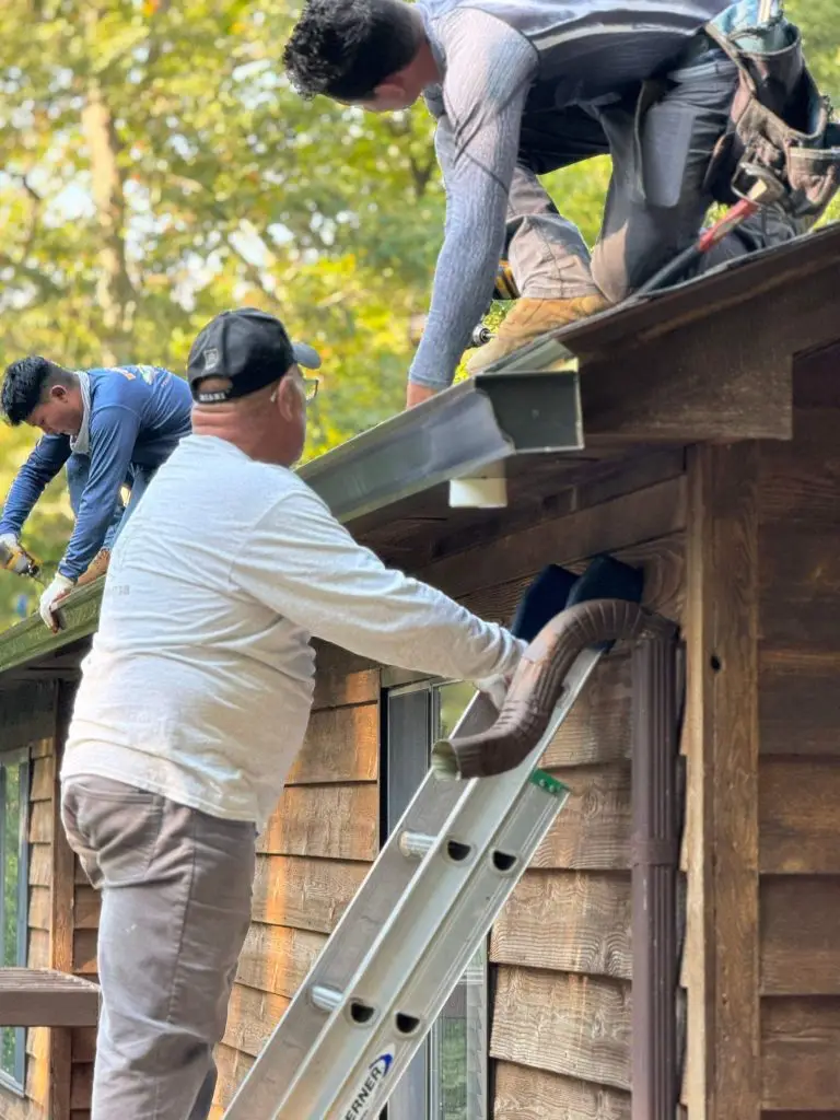 Worker on a ladder inspecting the eave of a brick home