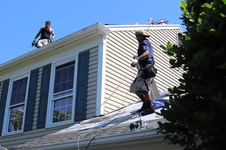 Roofers working beside a sided wall and roof junction
