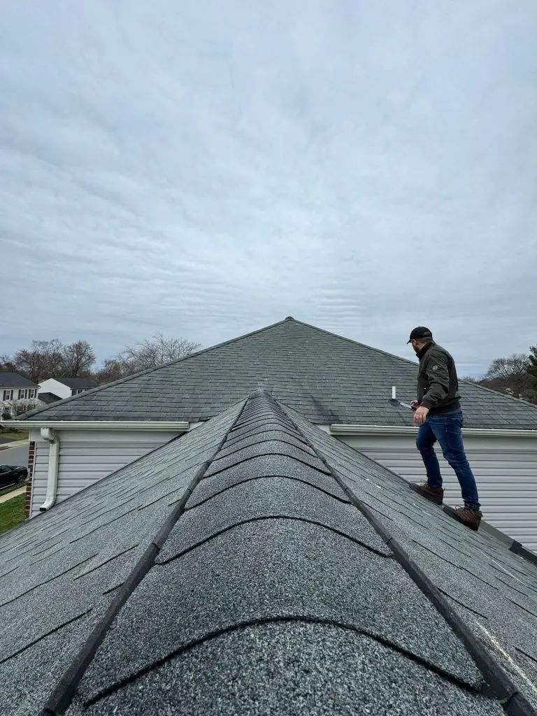 Roofer standing beside the ridge of a shingle roof